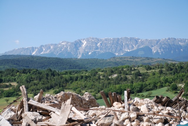 Macerie in primo piano e sullo sfondo, la Piana di Navelli e la catena del Gran Sasso