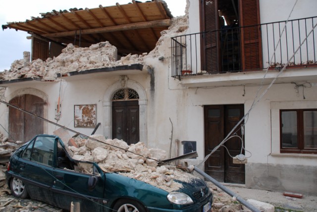 Una autovettura in primo piano completamente sommera dalle macerie di un edificio crollatole addosso